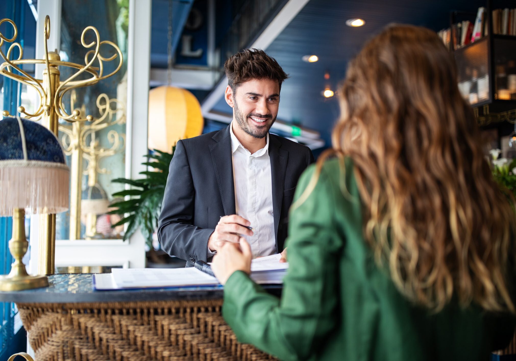Male hotel receptionist helping a woman guest in checking in process. Woman in hotel check-in at reception talking with the concierge at front office.